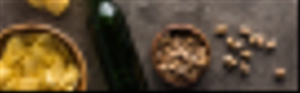 tiro panorâmico de garrafa de cerveja perto de tigelas com pistácios e batatas fritas na superfície texturizada marrom
 - Foto, Imagem