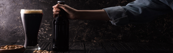 vista ritagliata dell'uomo che tiene la bottiglia vicino al vetro di birra scura e ciotole con noci sul tavolo di legno
 - Foto, immagini