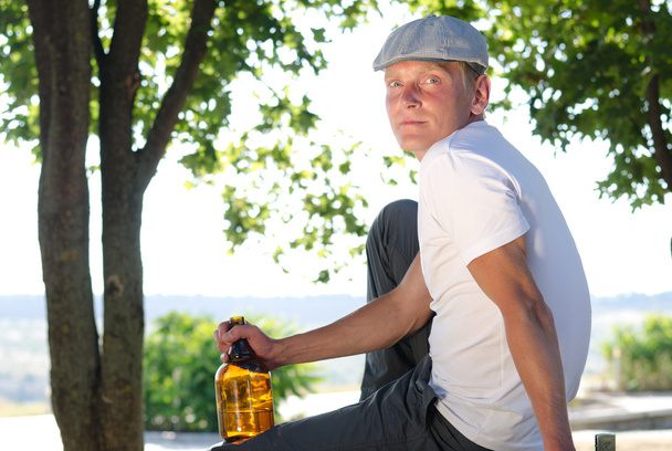 Homem sentado relaxando com uma garrafa de álcool
 - Foto, Imagem