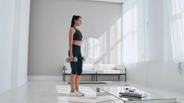 A woman at home on a Sunny day in the living room lunges back with dumbbells in her hands. Healthy lifestyle, daily exercise at home - Footage, Video
