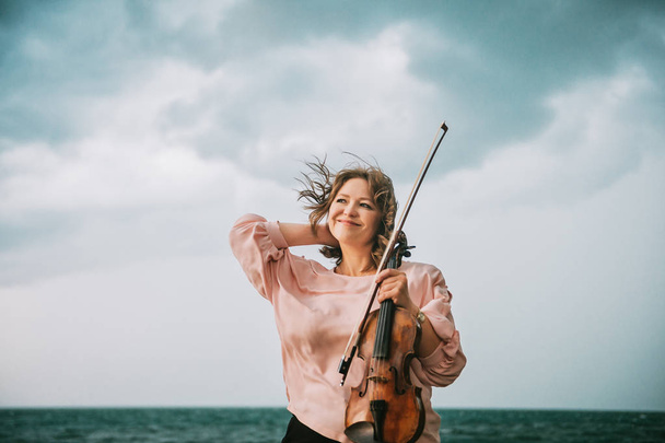 Outdoor portrait of beautiful woman with violin, dark rainy day - Photo, Image