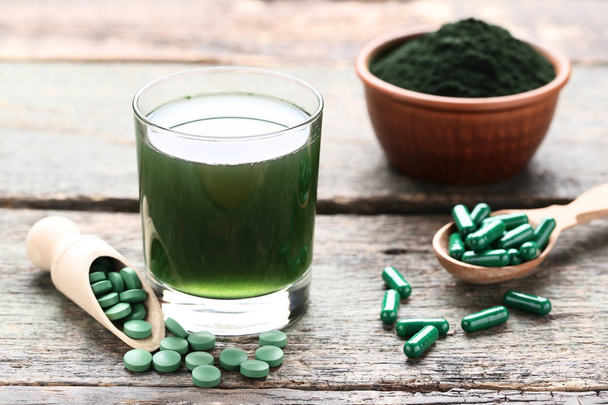 Spirulina drink and pills with powder in bowl on grey wooden tab - 写真・画像