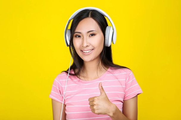 Beautiful woman with headphones showing thumb up on yellow backg - Valokuva, kuva