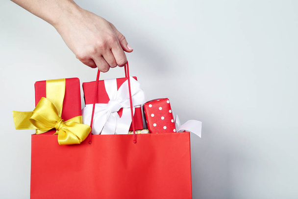 Female hand holding shopping bag with gift boxes on grey backgro - 写真・画像
