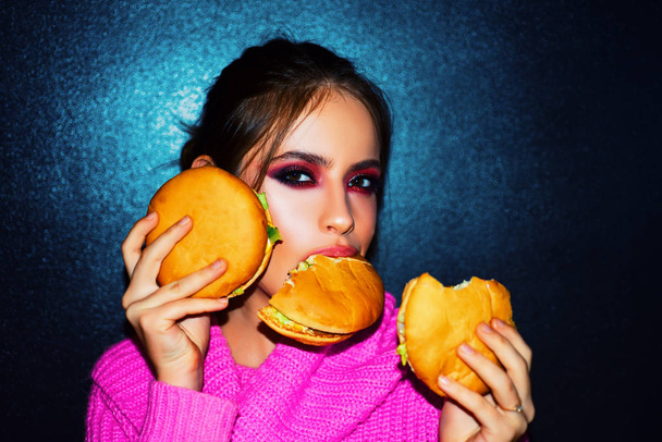 Fashion, beauty.Sexy woman with perfect makeup eating hamburgers. Female beauty visage concept. - Zdjęcie, obraz