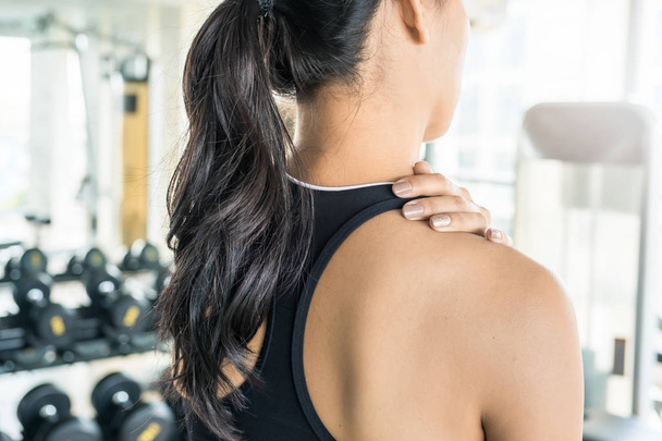 Asian woman holding her neck at the gym. Shoulder or back injury during training - Фото, зображення