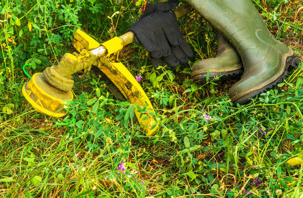 Бензиновый газонный триммер на зеленой траве и сапогах
. - Фото, изображение