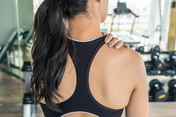 Mulher asiática segurando o ombro no ginásio. Lesão no ombro ou nas costas durante o treino
 - Foto, Imagem