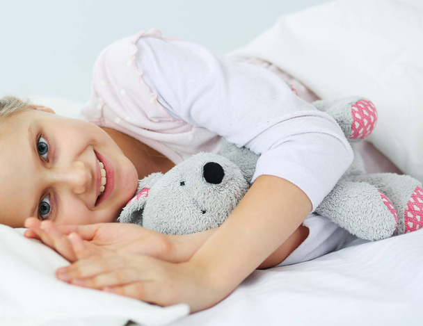 Child little girl sleeps in the bed with a toy teddy bear. - Photo, Image