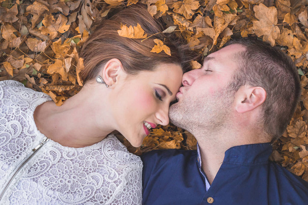 Paar liggend op de grond bedekt met gele herfst bladeren. - Foto, afbeelding