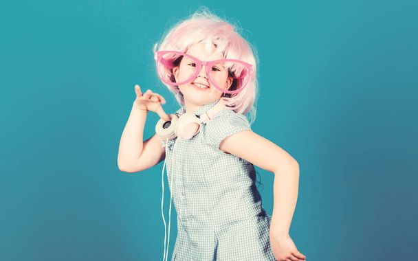 Small girl headphones pink wig dancing. Child using technology for fun. Modern headphones. Energy motion dance. Inspired by music. Little kid listening music. Cute kid with headphones blue background - Fotó, kép