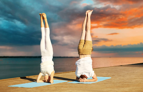 couple making yoga headstand on mat outdoors - Foto, afbeelding