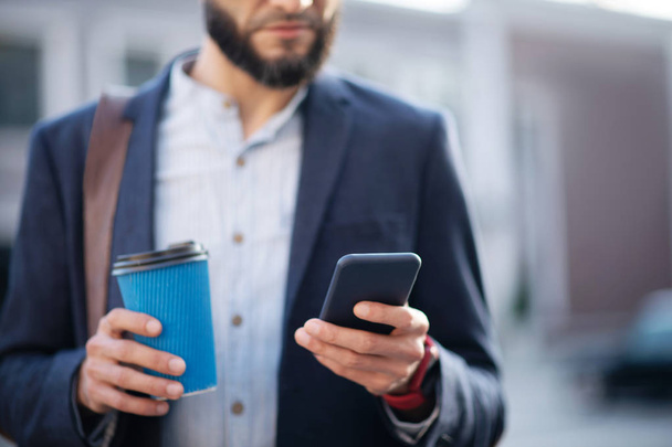 Bearded businessman reading e-mail on phone and holding coffee cup - Foto, afbeelding