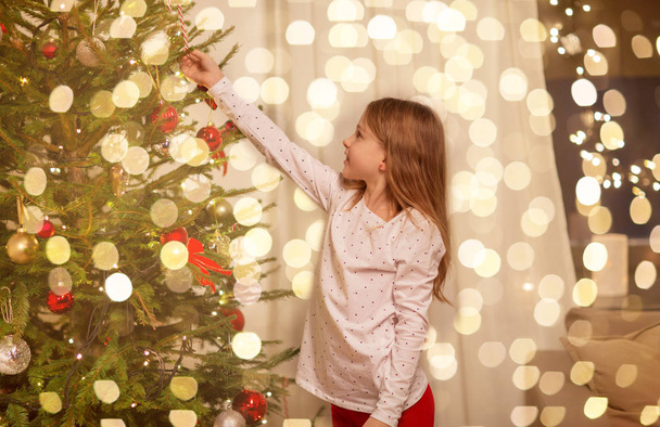 happy girl in red dress decorating christmas tree - Фото, изображение
