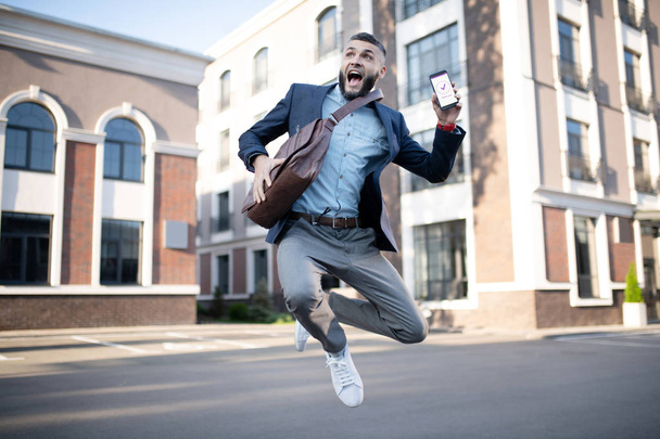 Handsome man jumping after reading message from company - Фото, зображення