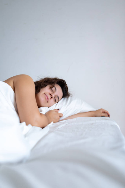 jonge mooie Kaukasische vrouw slapen in bed met witte lakens - Foto, afbeelding