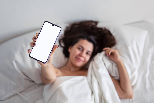 mujer acostada en la cama mostrando el teléfono con pantalla blanca
 - Foto, Imagen