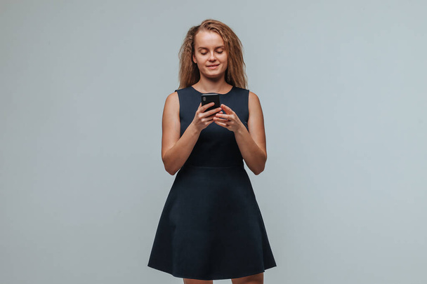 Дівчина в блакитній сукні вводить повідомлення в телефоні на сірому
 - Фото, зображення