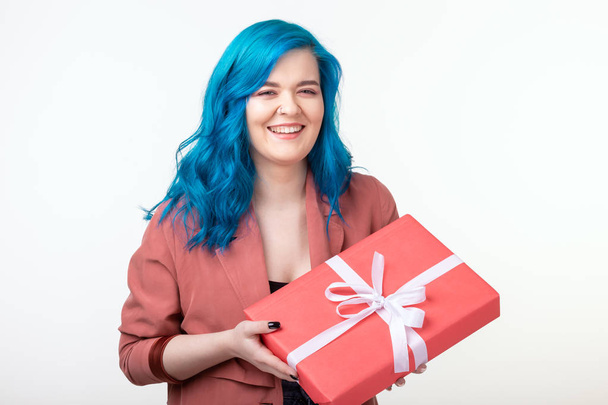 People, holidays and fashion concept - Surprising woman with blue hair holding a gift box on white background - Foto, immagini