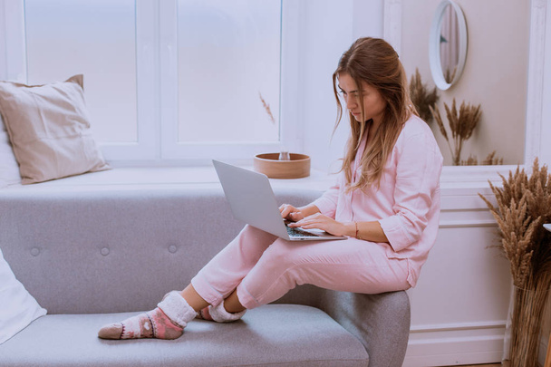 Утром леди в розовой пижаме работает в гостиной на ноутбуке, современный дизайн
 - Фото, изображение