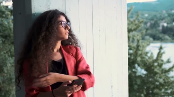 Νεαρή γυναίκα με κόκκινο μπουφάν στέκεται γέρνει πίσω στον τοίχο και παίρνοντας selfie - Πλάνα, βίντεο