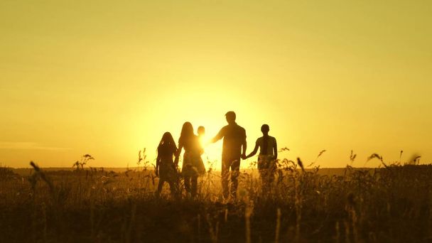 gelukkig familie wandelingen in veld in zonsondergang licht. vader moeder en dochters lopen in het Park in het licht van de zon. kinderen en ouders reizen op vakantie. gelukkige vader draagt een kind - Foto, afbeelding