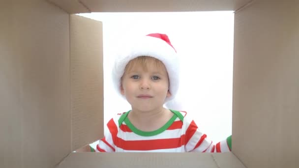Happy child looking into the box. Funny surprised kid unpack Christmas gift box. Xmas holiday concept. Low angle view. Slow motion - Πλάνα, βίντεο