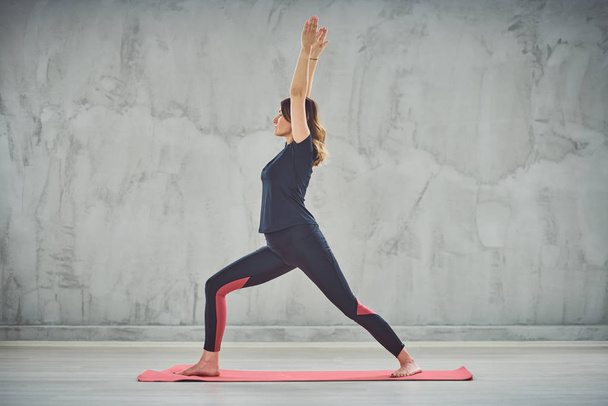 Side view of Caucasain brunnette standing on the mat in Crescent Lunge yoga posture. - Fotó, kép