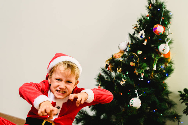 Toddler boy with funny face wearing Santa costume trying to scar - Φωτογραφία, εικόνα