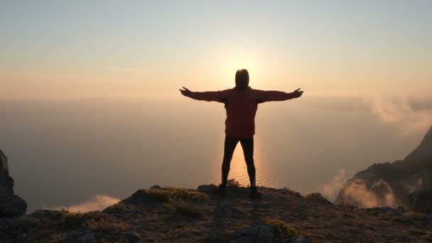 クリミアの高い山から海の上に美しい劇的なカラフルな夕日を観察する若者の腕のシルエットは伸びた. - 映像、動画