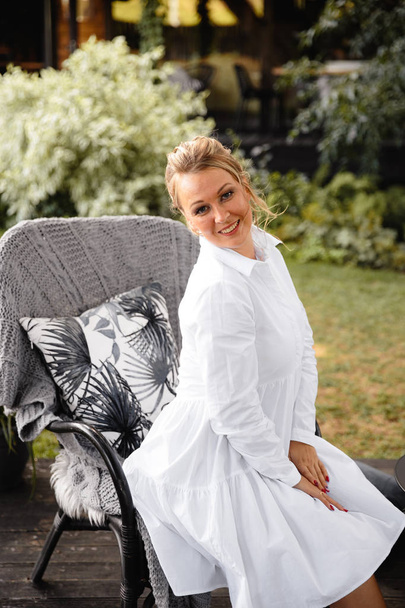 Beautiful woman in white portrait in an outdoor cafe garden in summer or early autumn with green grass and trees - Foto, afbeelding