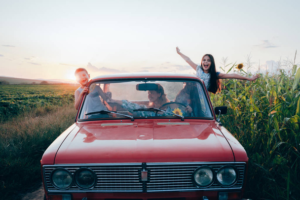 Happy playful family traveling together by the car, beautiful young mom driving and her children got out the car windows and having fun, sunset on the background - Zdjęcie, obraz