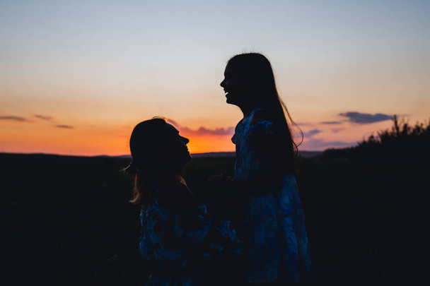 Silhouette of the happy mom and daughter on sunset background - Photo, image