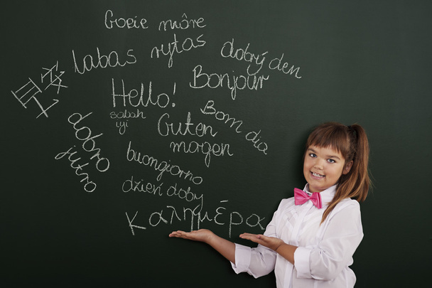 Schoolgirl presenting foreign phrases on blackboard - Foto, imagen