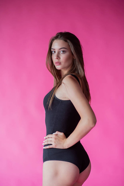 Beautiful fashionable girl with long hair in a black T-shirt. Girl in the studio on a pink background - Foto, imagen