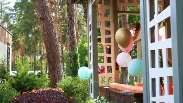 Bunch of different colorful helium air balloons playing on wind tied to wooden outdoor gazebo terrace as decoration for children bithday party. Anniversary celebration decor design - Footage, Video