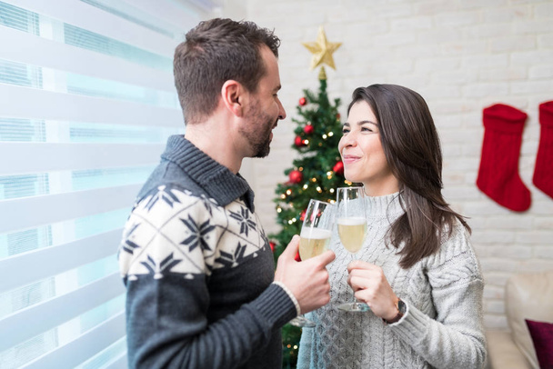 Casal adulto médio comemorando o Natal enquanto brinda flautas de champanhe em casa
 - Foto, Imagem