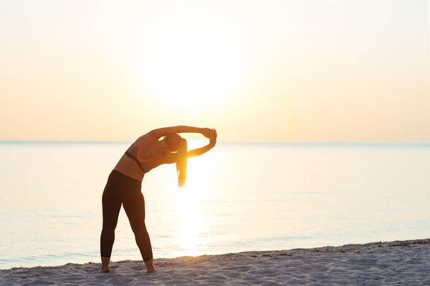 Young woman at the beach in sunset stretching after workout - Фото, изображение