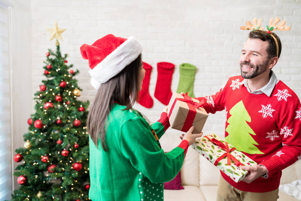 Happy couple swapping gifts at home during Christmas celebrations - Photo, Image