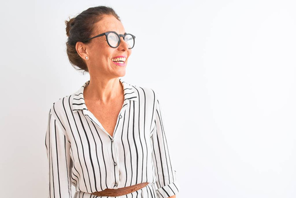 Middle age businesswoman wearing striped dress and glasses over isolated white background looking away to side with smile on face, natural expression. Laughing confident. - Photo, Image