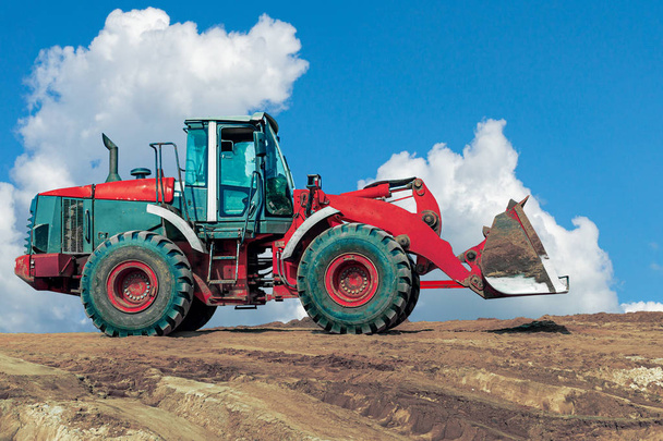 青空に対する建設現場の赤い掘削機。土工作業中の砂場のホイールローダー - 写真・画像