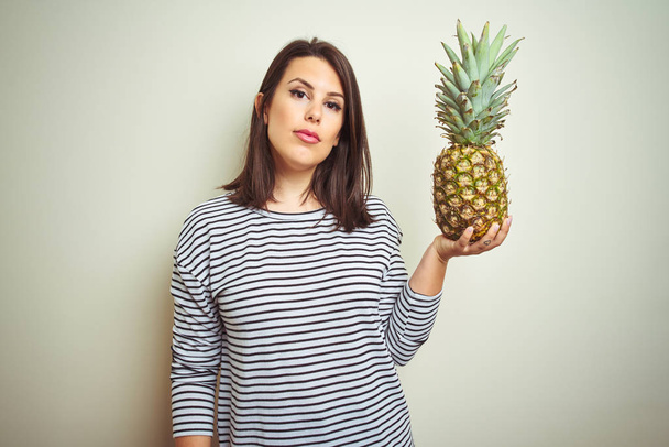Fiatal gyönyörű nőt gazdaság trópusi gyümölcs ananász mint elszigetelt háttér egy magabiztos kifejezése okos arc gondolkodó komoly - Fotó, kép
