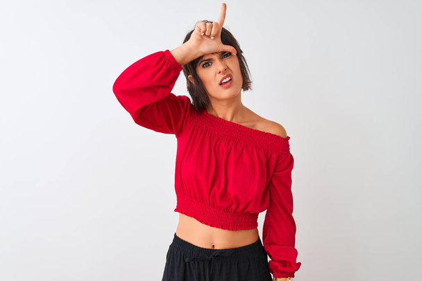 Mladá krásná žena na Rudém letním tričku, stojící nad osamělým bílým pozadím, která si dělá legraci z lidí s prsty na čele, děkuje a uráží. - Fotografie, Obrázek