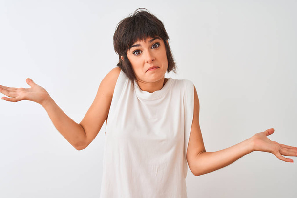 Young beautiful woman wearing casual t-shirt standing over isolated white background clueless and confused expression with arms and hands raised. Doubt concept. - Fotoğraf, Görsel