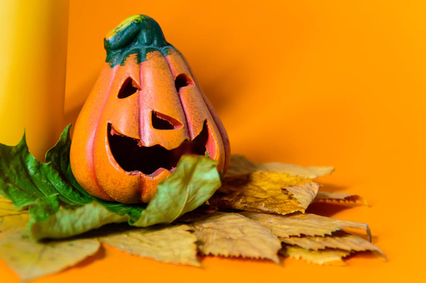 Close-up de cerâmica decorativa Halloween abóbora jack-o-lanterna em folhas secas de outono e vela amarela
. - Foto, Imagem