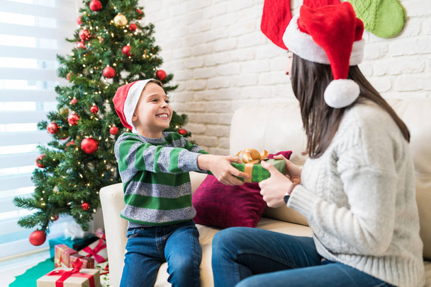 Podekscytowany mały dzieciak daje prezent mamie w domu podczas świąt Bożego Narodzenia - Zdjęcie, obraz