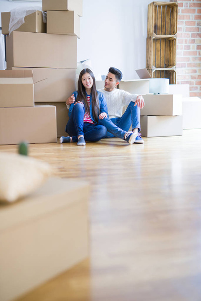 Young asian couple sitting on the floor of new house arround cardboard boxes relaxing and smiling happy - Φωτογραφία, εικόνα