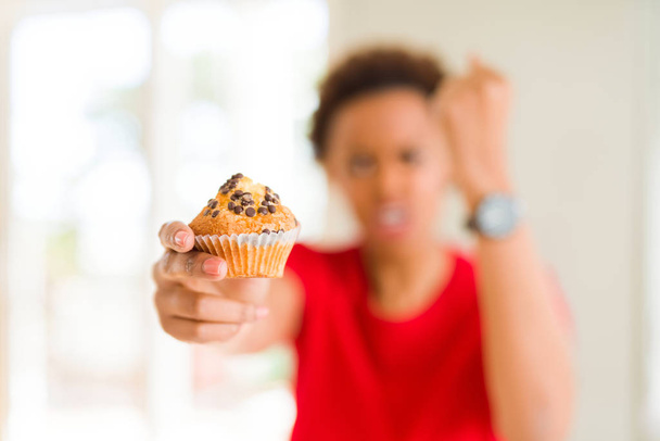 Young african american woman eating chocolate chips muffins annoyed and frustrated shouting with anger, crazy and yelling with raised hand, anger concept - Zdjęcie, obraz