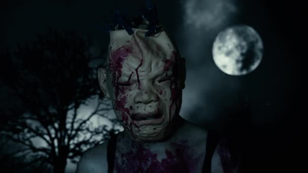 Een enge man in een bloedend masker op een begraafplaats, tegen de achtergrond van een volle maan en dode boom in de schemering.. Horror karakter concept. Enge plaatsen. Halloween achtergrond - Video