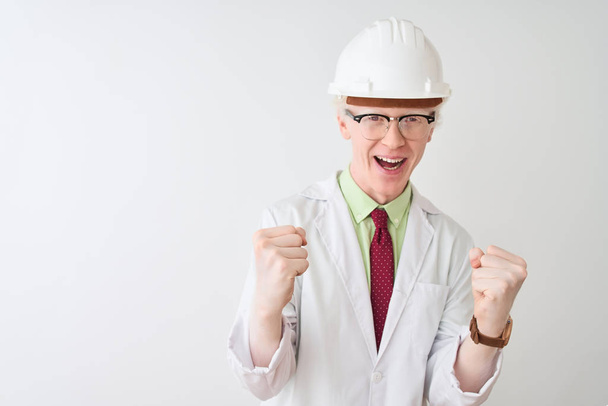 Hombre científico albino con gafas y casco de pie sobre fondo blanco aislado celebrando sorprendido y sorprendido por el éxito con los brazos levantados y los ojos abiertos. Concepto ganador
. - Foto, imagen